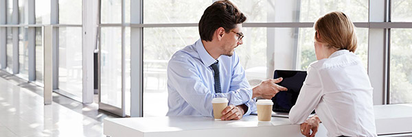 Financiación internacional - Reunión de negocios entre un hombre y una mujer de negocios con camisa, frente a un portátil hablando y tomando café